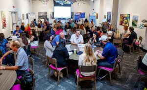 HDMS22-86 Round Table Whole Room Jenn Edits Conference room full of people at tables talking together