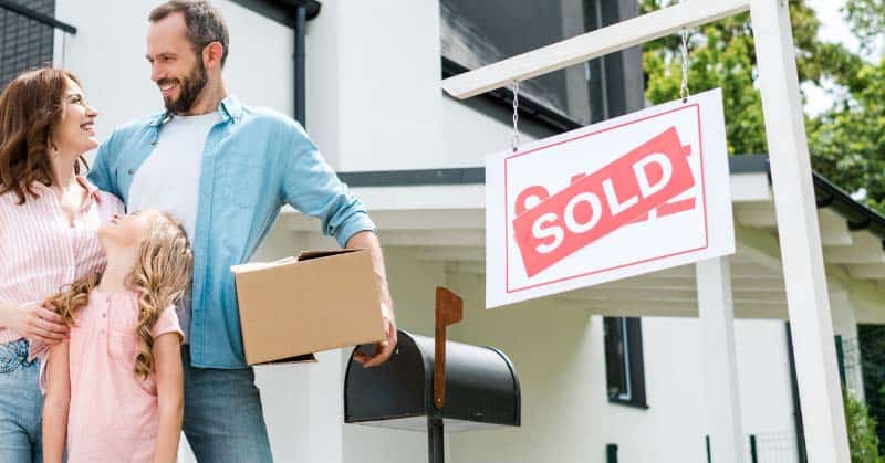 Family That Just Bought a New Home Family standing in front of a home with a "Sold" sign